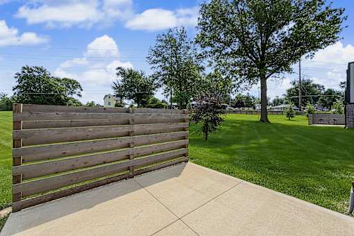 A wooden fence in the foreground with a green lawn and trees in the background.