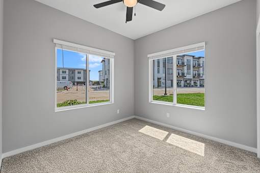A room with a ceiling fan and two windows overlooking a street.