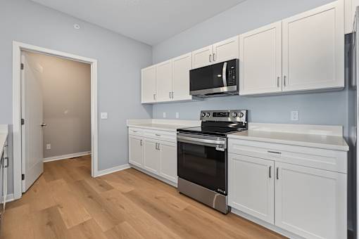 A kitchen with white cabinets and a black microwave.