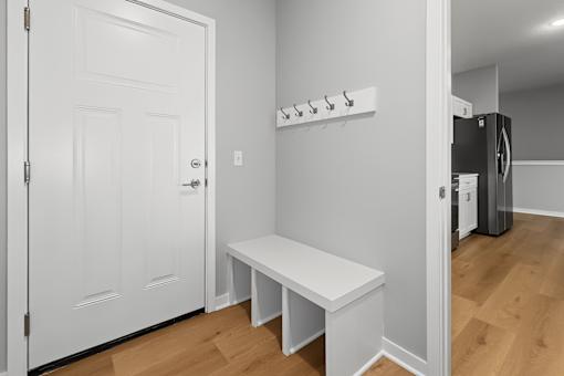 A white door is open to a room with a bench and a coat rack.