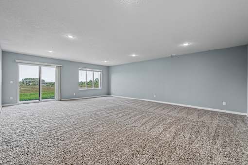 A large empty room with carpeted floor and two windows.
