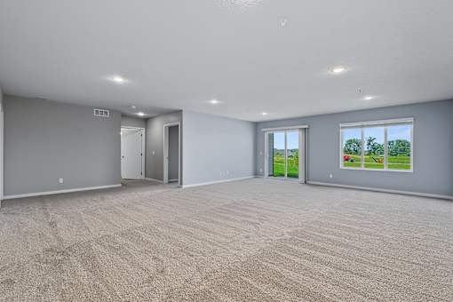 A large empty room with carpeted floor and a view of greenery outside the window.