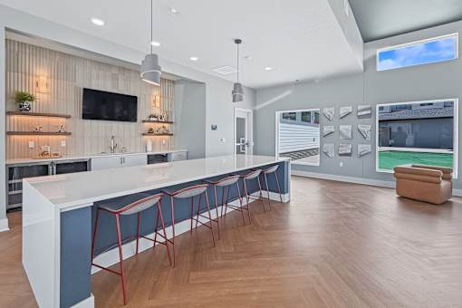 A modern kitchen with a long white island and red barstools.