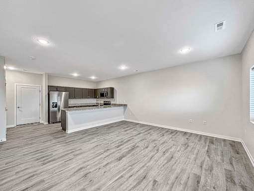 an empty living room and kitchen with a refrigerator and a sink at Forge65, Pleasant Hill, 50327