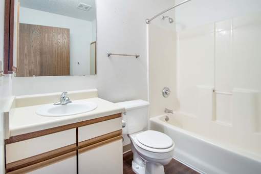 A white toilet sits next to a sink in a bathroom at Hunters Run Apartments, Iowa, 50208