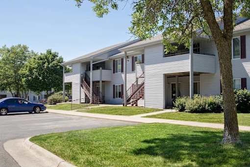 A blue car is parked on the street in front of a white house at Hunters Run Apartments, Newton