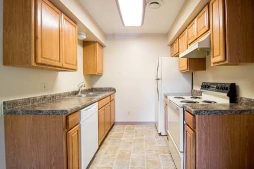 A kitchen with wooden cabinets and a white dishwasher at Hunters Run Apartments, Iowa, 50208