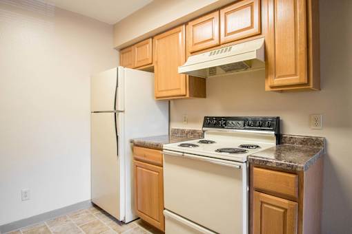 A kitchen with a white refrigerator, a white stove, and wooden cabinets at Hunters Run Apartments, Newton