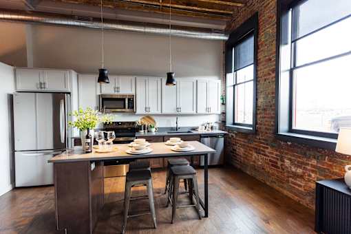 A kitchen with a table and chairs in front of a brick wall.at Plant 1 Lofts, Iowa, 50208