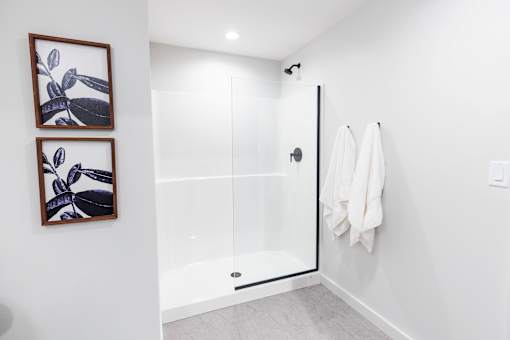 A white bathroom with a glass shower door and two framed pictures on the wall.at Plant 1 Lofts, Iowa   