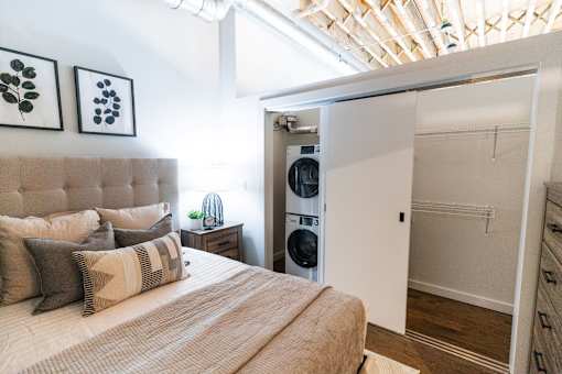A bedroom with a bed, pillows, and a washing machine in the closet.at Plant 1 Lofts, N. Newton, 50208  