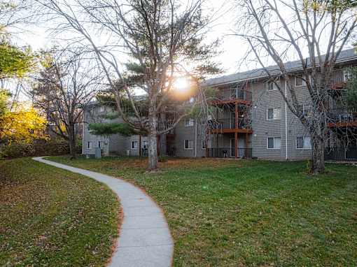 A sunlit pathway leads to a building with a balcony at Rosemont Place Apartments, Des Moines, 50320