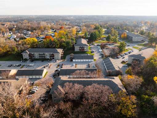 A parking lot is surrounded by trees and buildings. at Rosemont Place Apartments, Des Moines