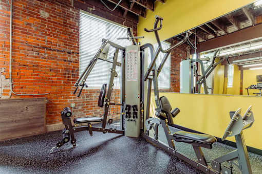 A gym with a red brick wall and a variety of exercise equipment at Spaulding Lofts Apartments, Grinnell, IA, 50112