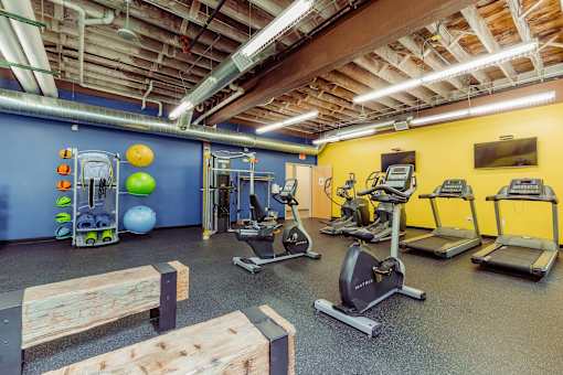 A gym with a variety of exercise equipment including treadmills, stationary bikes, and weight machines at Spaulding Lofts Apartments, Iowa, 50112