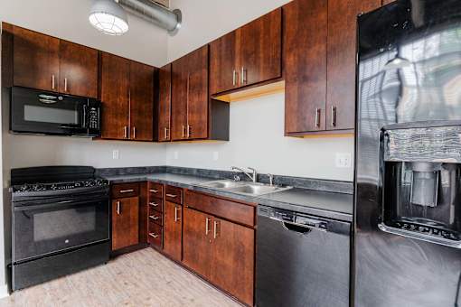 A kitchen with wooden cabinets and black appliances at Spaulding Lofts Apartments, Grinnell, IA, 50112