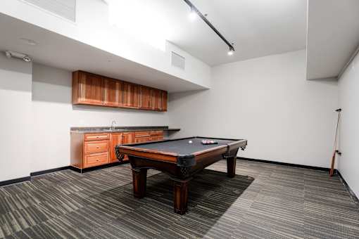 A pool table is in the middle of a room with a wooden cabinet and a pool cue on the right.