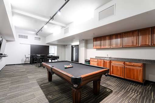 A pool table is in the middle of a room with a black chair and a TV.