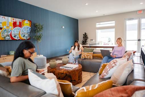 Three women are sitting on a couch in a room with a large painting on the wall.