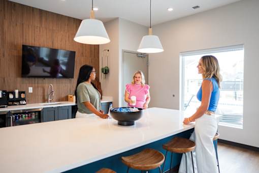 Three women are standing in a kitchen with a bowl on the counter.