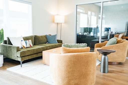 A living room with a green couch, a brown ottoman, and a glass door.