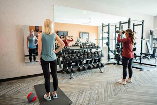 A woman is working out in a gym with a mirror and various exercise equipment.