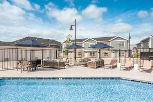 A pool surrounded by chairs and umbrellas with a building in the background.