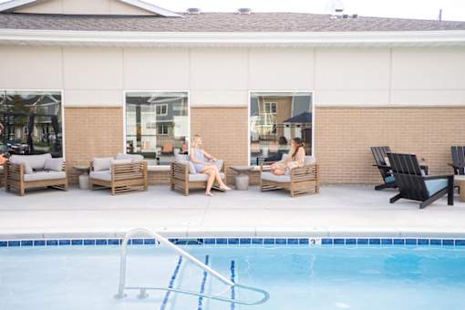 Two women sitting on lounge chairs by a pool.