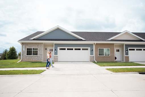 A woman stands in front of a grey house.