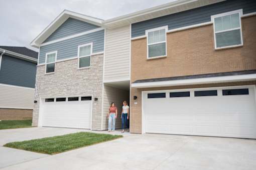 Two people standing in front of a house with a garage door.