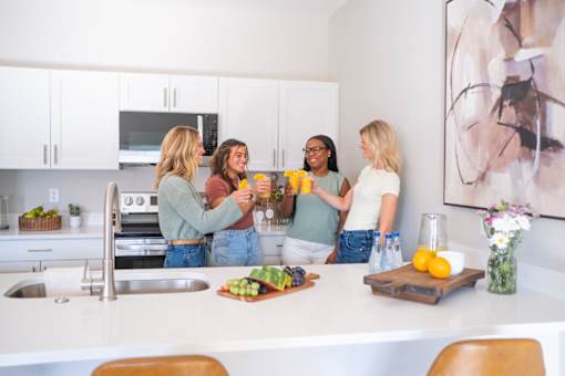Four women are standing in a kitchen and having a conversation.