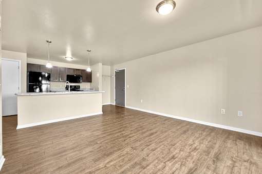 A large open living room with wooden flooring and a kitchen area in the background at Melbourne Apartments in Des Moines, Iowa 50320.
