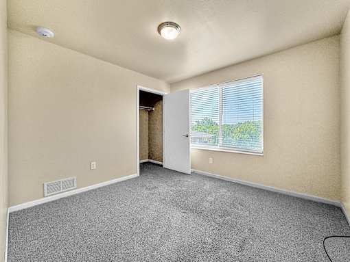 A room with a carpeted floor and a window with blinds.