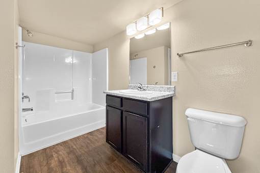 A bathroom with a toilet, counter space with black cabinets, and tub and shower combination at Melbourne Apartments in Des Moines, Iowa 50320.