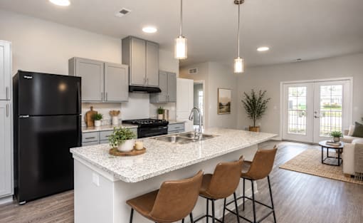 A modern kitchen with a black fridge, white countertops, and wooden chairs.
