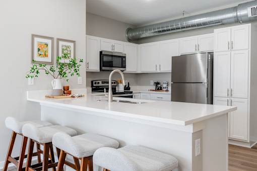 a kitchen with a large island with stools and a stainless steel refrigerator at Converge NW, Waukee Iowa  