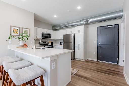 A kitchen with white cabinets and a white island with three stools at Converge NW, Waukee, 50263