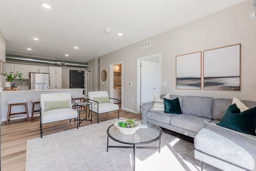 A living room with a grey couch, a coffee table, and a dining table with chairs.at Converge NW, Waukee  