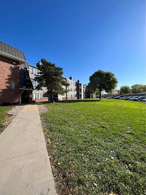 A grassy area in front of a building with a sidewalk at Penbrooke Place Apartments, South Dakota, 57106