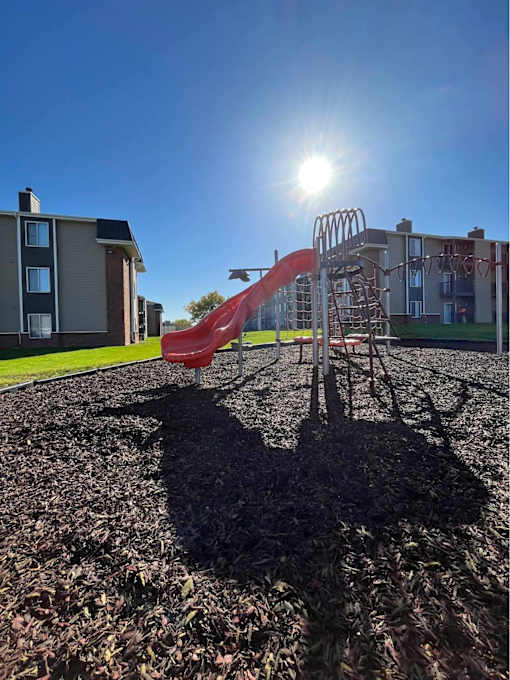A playground with a red slide and a person's shadow on the ground at Penbrooke Place Apartments, Sioux Falls, SD, 57106