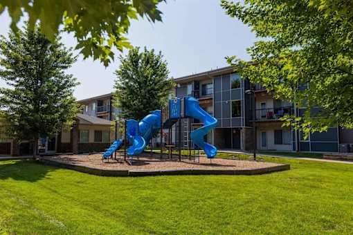 A blue slide in a playground in front of a building.