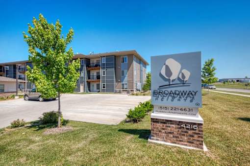 A sign for Broadway Apartments stands in front of a building with a tree to the left.
