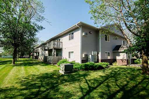 A house with a grey siding and a balcony is surrounded by green grass and trees at Peach Tree Apartments, Ankeny, IA