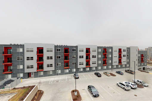 A large grey building with red accents and a parking lot in front at Vue Apartments, Des Moines