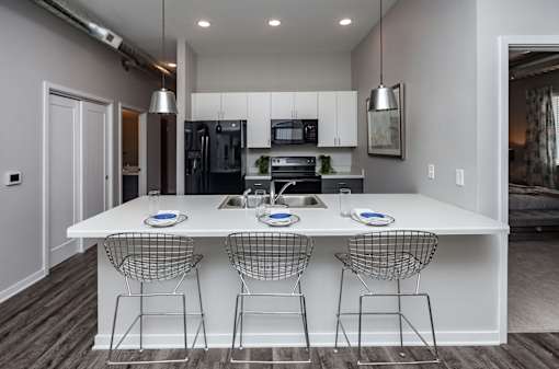 A modern kitchen with a white island and three chairs at Vue Apartments, Des Moines, IA