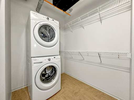 A white dryer and washer are stacked on top of each other in a small laundry room at The Des Moines Building Apartments, Iowa