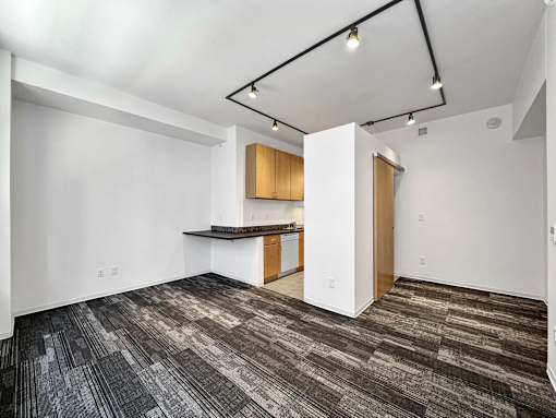 A room with a carpeted floor and a kitchenette at The Des Moines Building Apartments, IA, 50309
