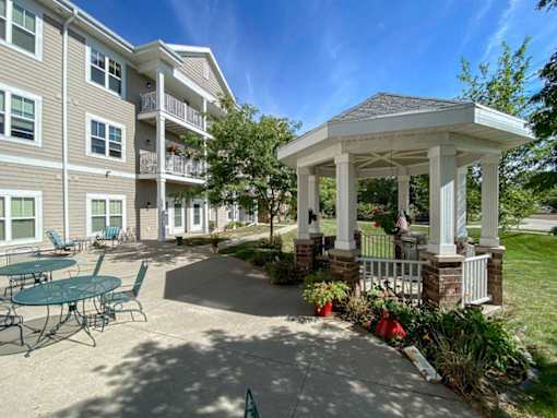 A gazebo is surrounded by a building and a patio with chairs.at Cornerstone Commons, Johnston, IA 50131  