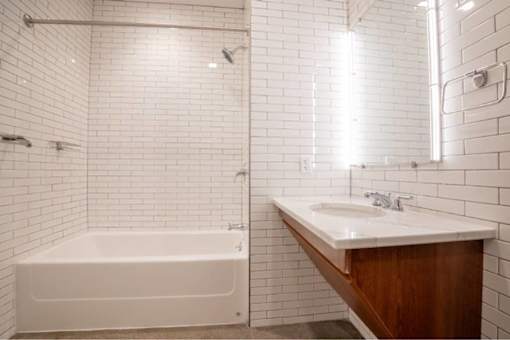 White tiled bathroom with a white bathtub, sink, and a white shower head at Clemens Building, Des Moines, 50309