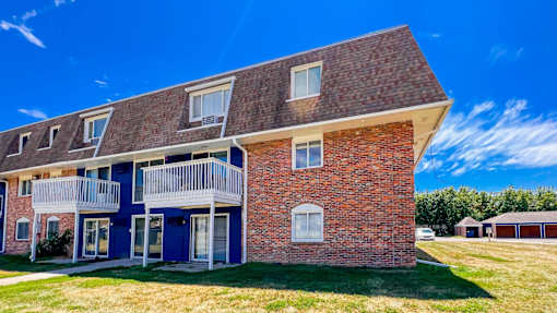 A red brick house with a blue door and white railings at The Hampton Meadows Apartments, Des Moines, IA